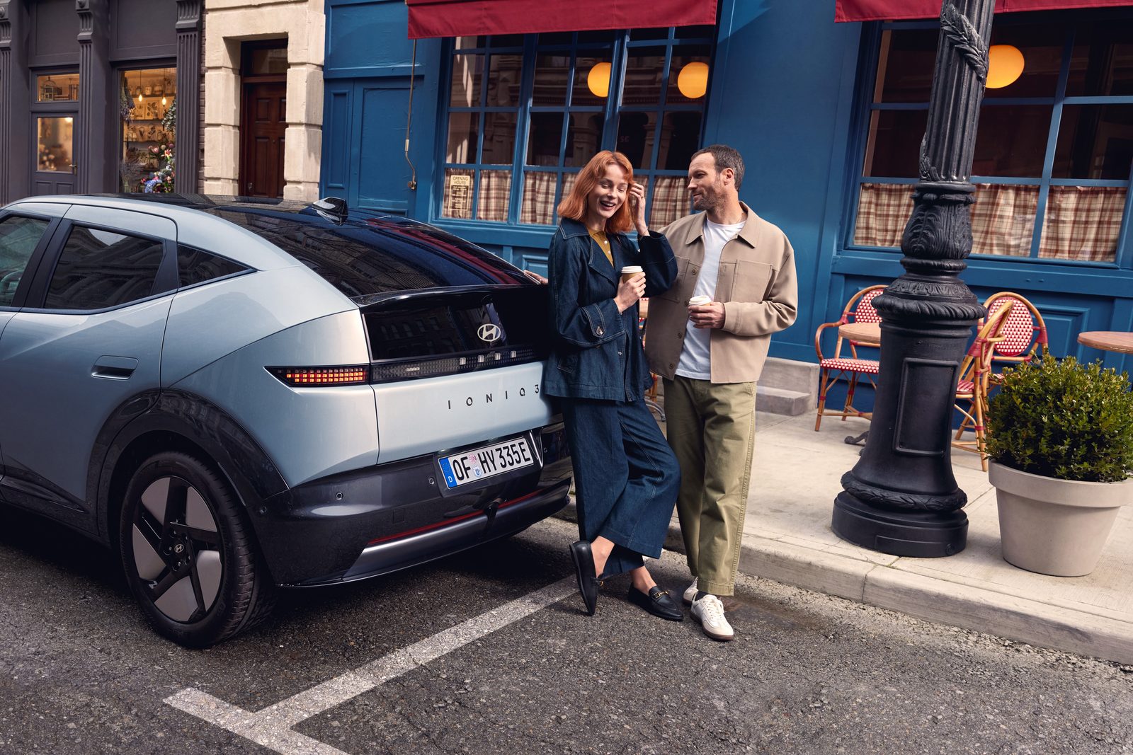 Hyundai IONIQ 3 Heckansicht Heckansicht des Hyundai IONIQ 3 mit zwei Personen vor einem Café